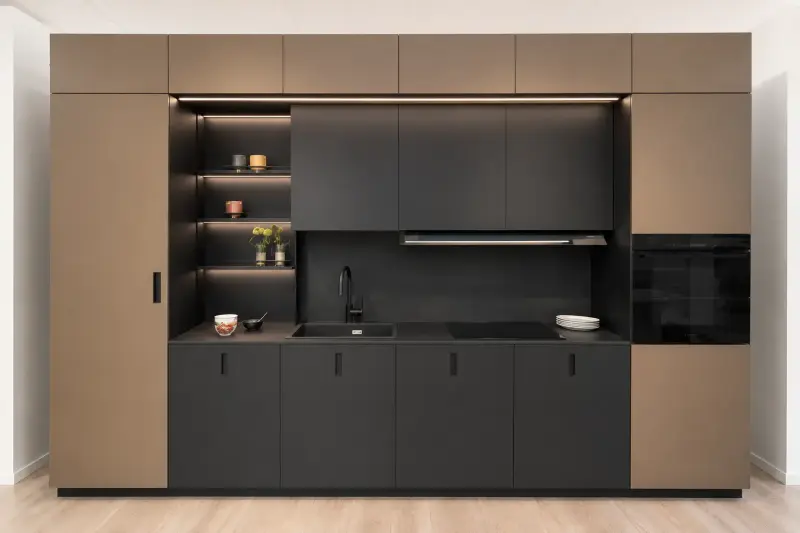 Cucina Monolith Chic: blocco compatto con finiture scure, colonne color bronzo e mensole illuminate.
