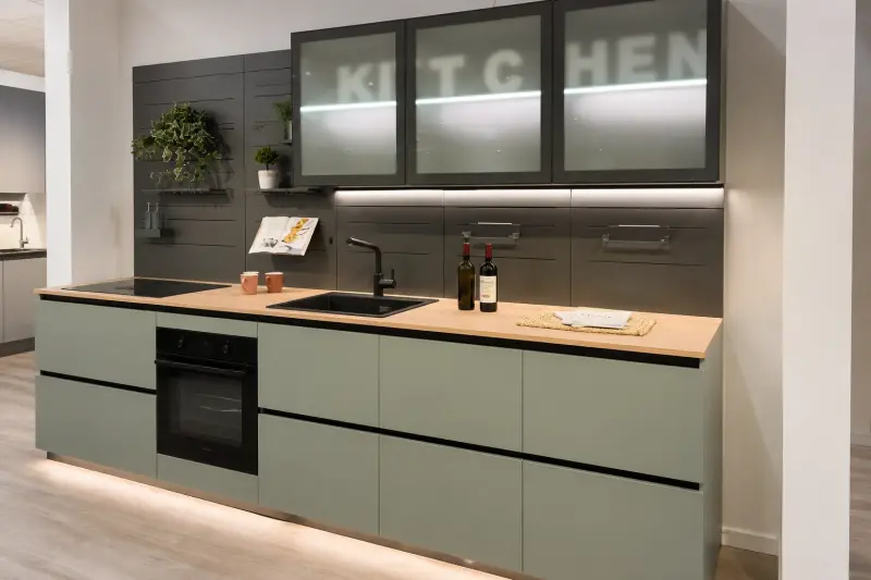 Cucina Urban Glass: pensili in vetro satinato illuminati, basi verde salvia opache e piano in legno.