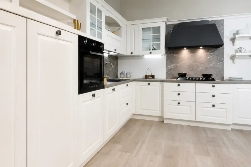 Cucina White Heritage: ante bianche lavorate, cappa scura e parete effetto marmo in stile classico.