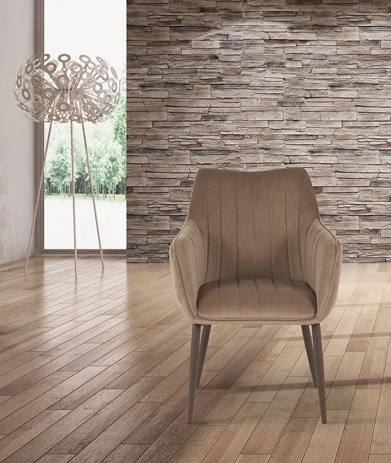 Poltrona beige su un pavimento in legno chiaro, addossata a una parete in pietra, accanto a una lampada da terra decorativa.