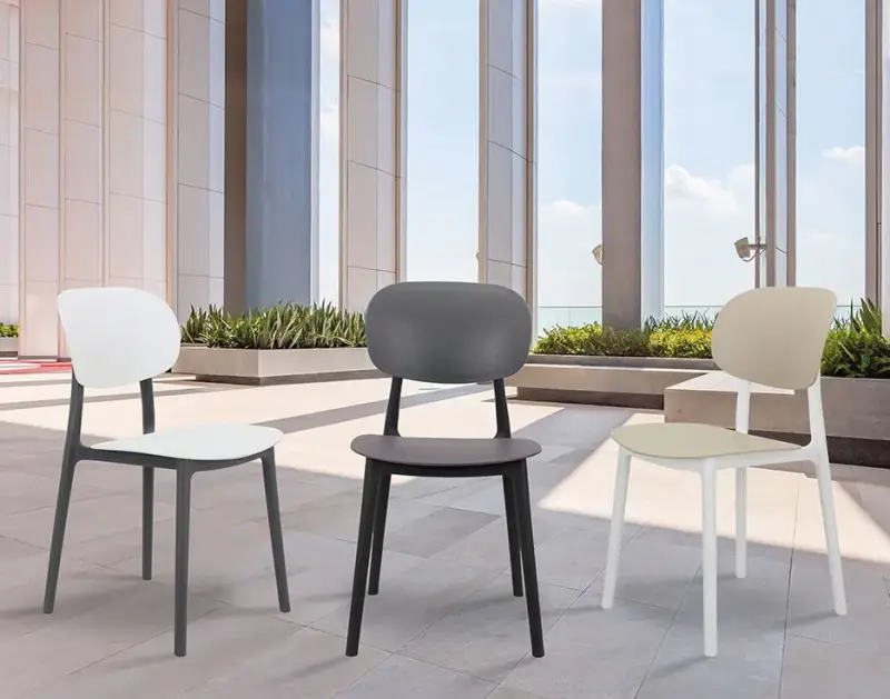 Tre sedie moderne – bianche, nere e color crema – su un patio accanto ad alte colonne e finestre.